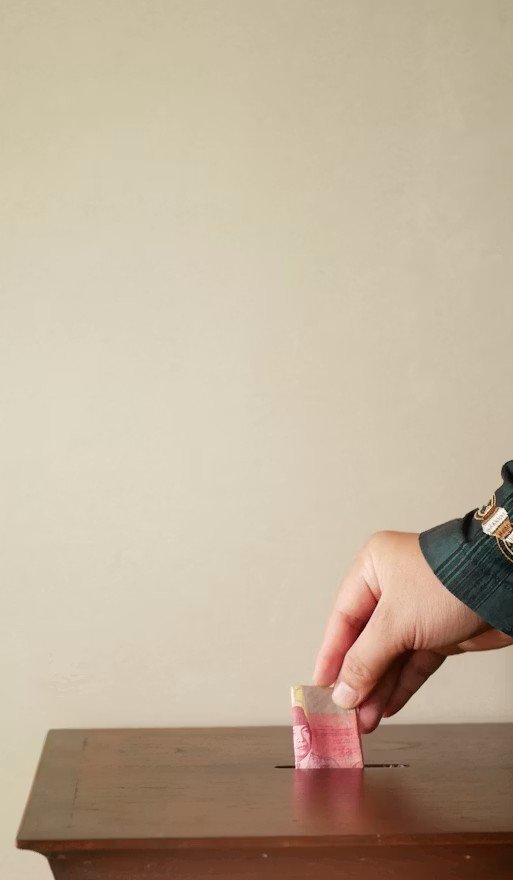 Main déposant un billet dans une boîte de collecte en bois